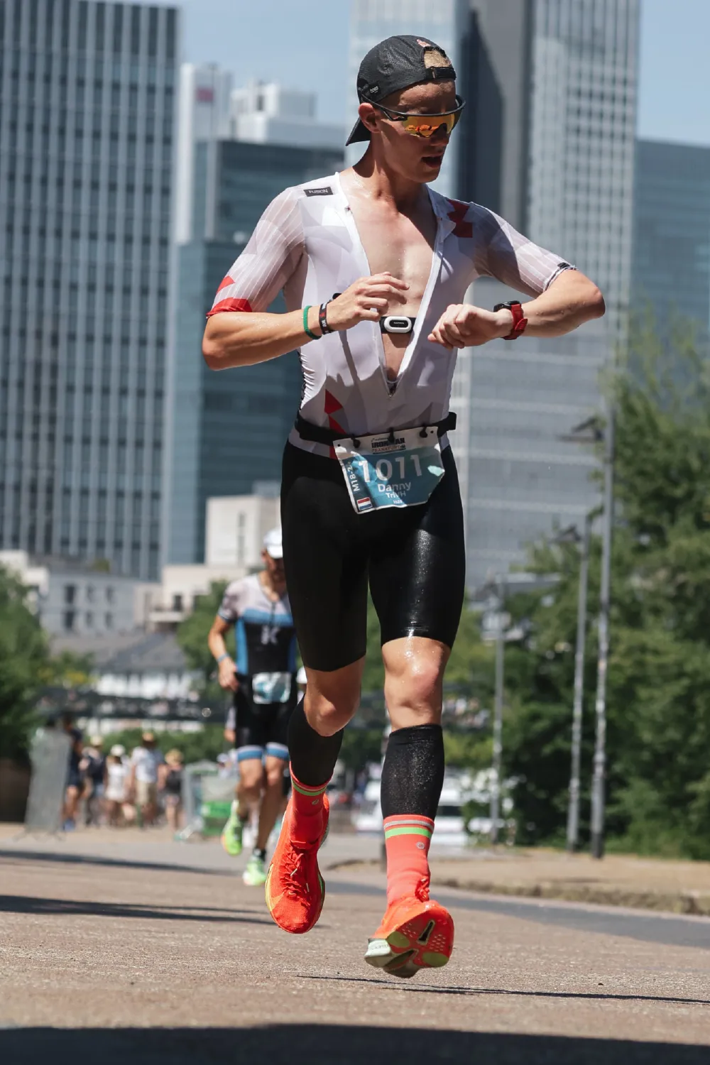 Danny Verdel checking the watch during the run, with the Frankfurt skyline behind, at Ironman Frankfurt 2026